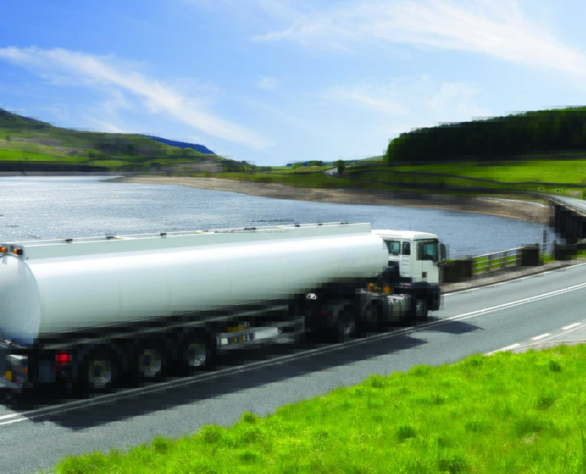 truck with tank driving on road curving around a pretty lake
