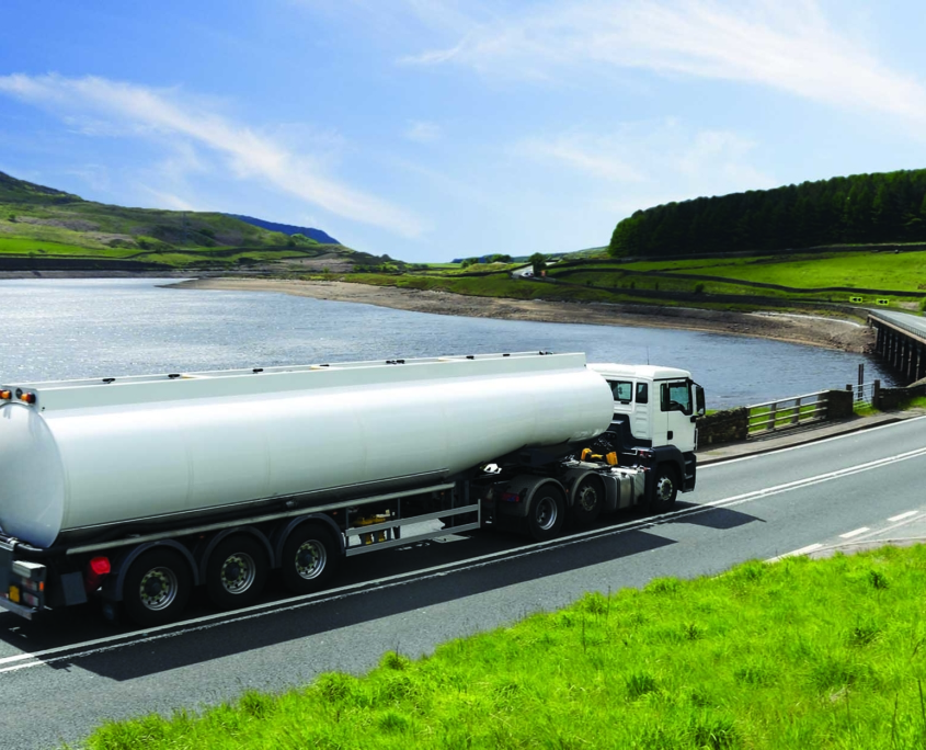 truck with tank driving on road curving around a pretty lake