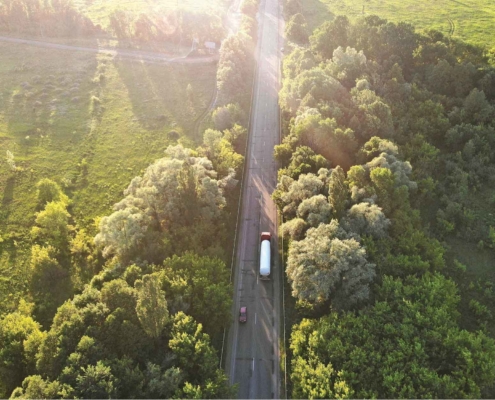 view from the sky looking down on a tanker truck driving on a road through a sunny forest