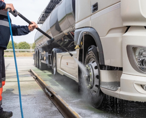 Worker cleaning tank truck with power washer